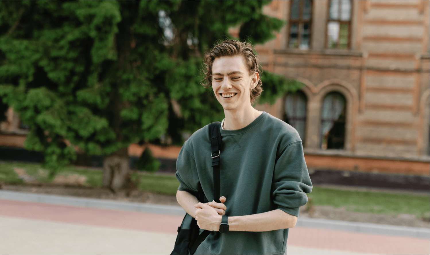 A college student wearing a backpack smiles on his way to class.