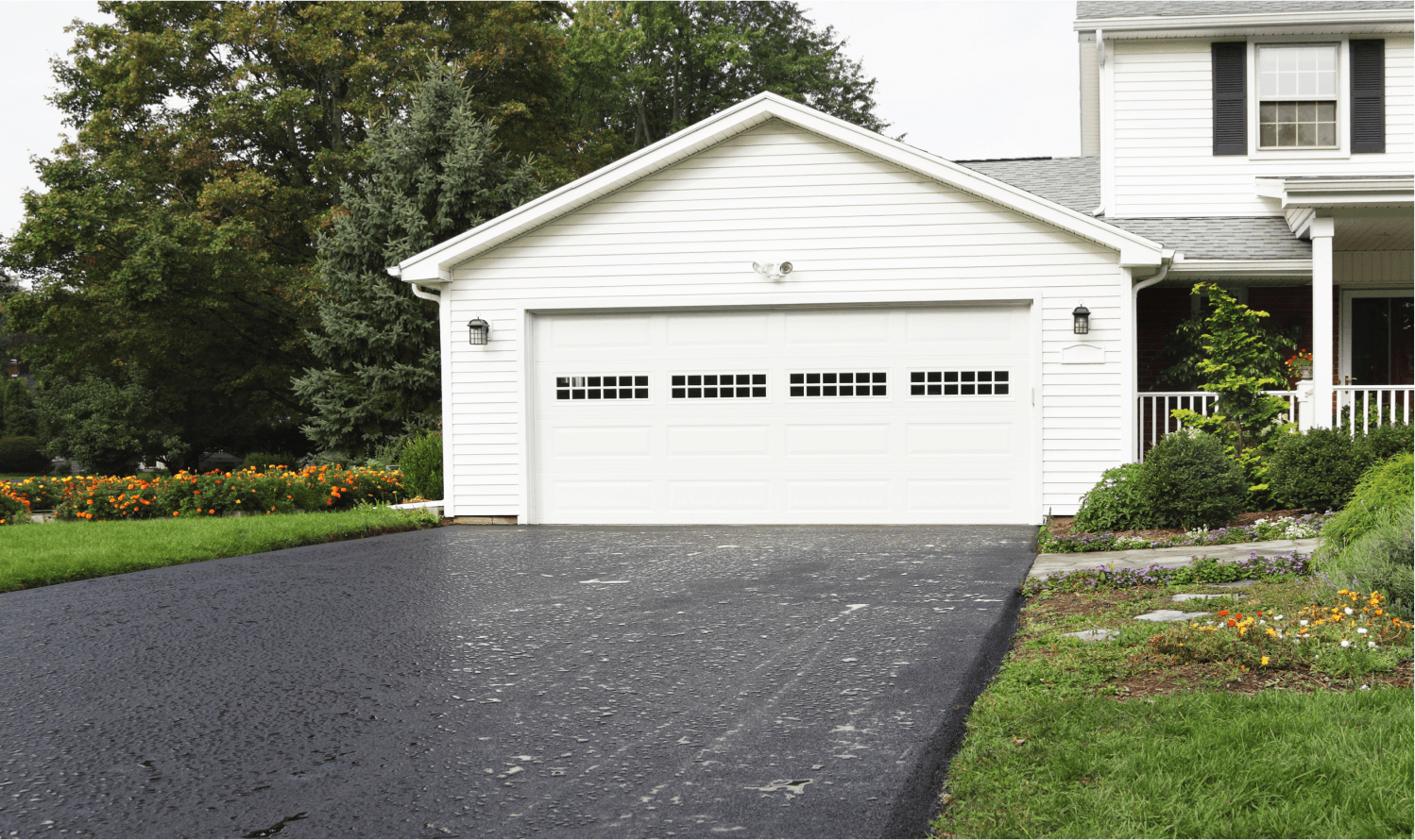 A white garage sits at the end of a blacktop driveway.