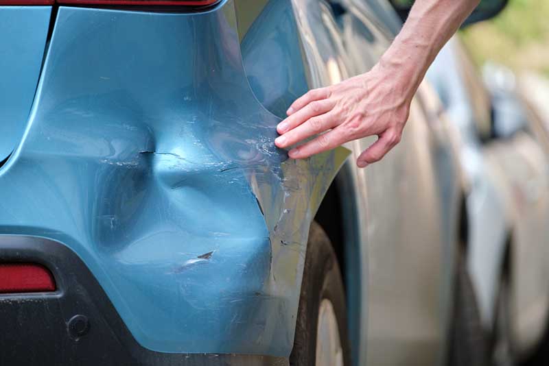 A man touches the damage on his car after a collision.