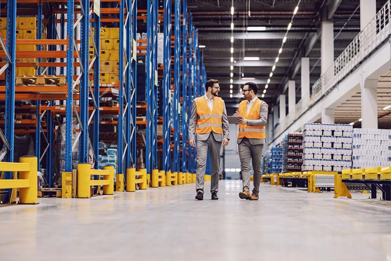Two workers in safety vests walk through a remote warehouse.