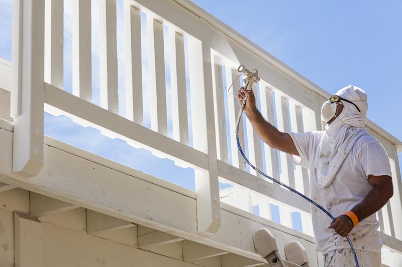 A professional painter sprays a porch railing with a paint sprayer.
