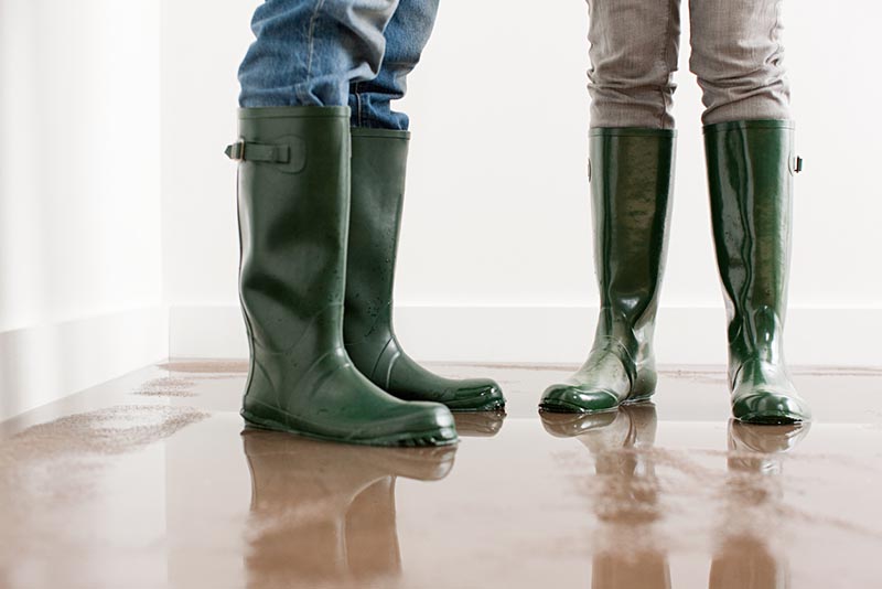 A flooded home with homeowners wearing rubber boots