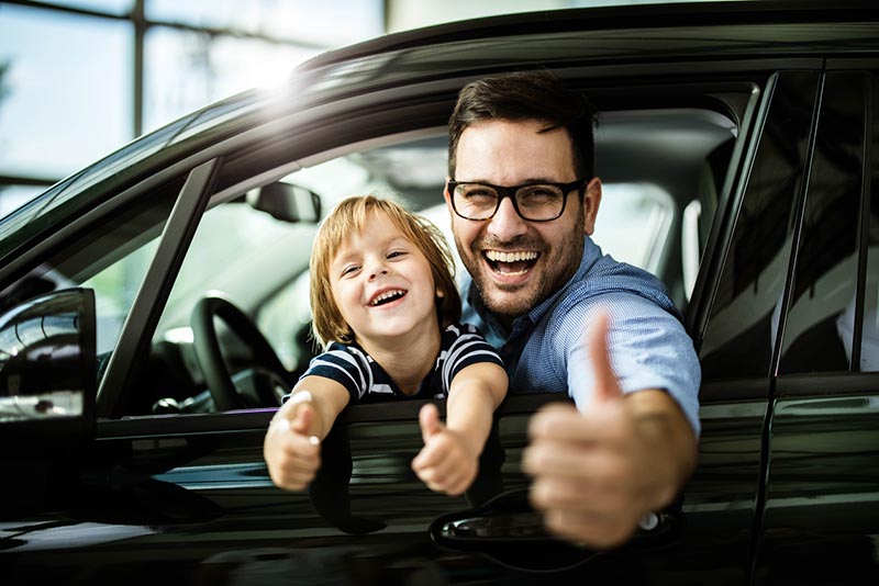 A father and son in a car giving thumbs up and celebrating the peace of mind of car insurance
