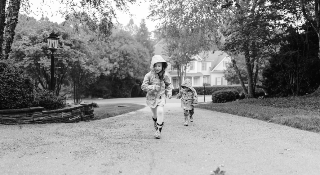 Two children in raincoats walking up a driveway.